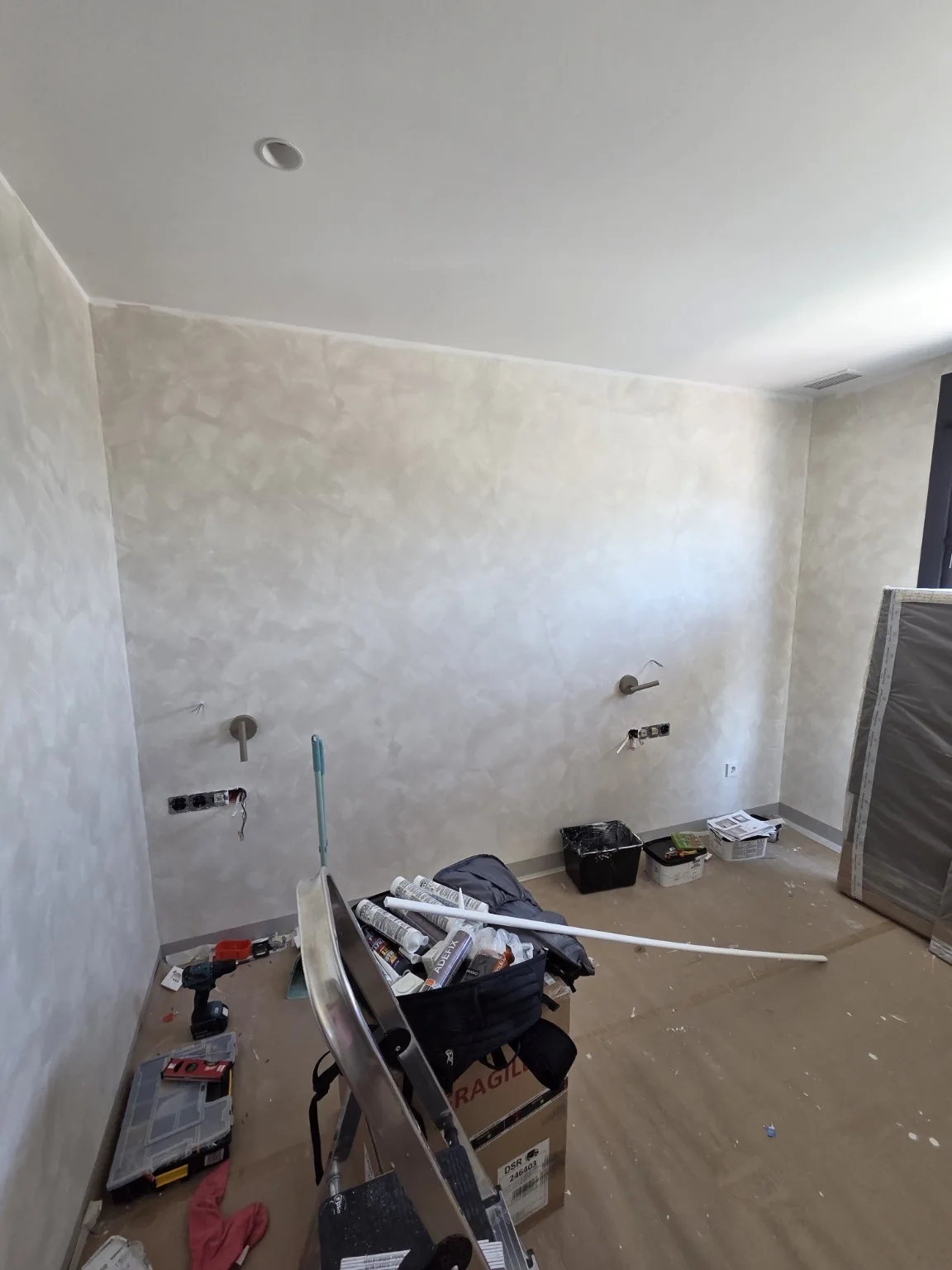 Ściana z efektem limewash podczas prac, z zabezpieczoną podłogą